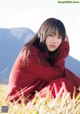 A woman in a red sweater sitting in a field.