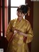 A woman in a yellow kimono standing by a window.