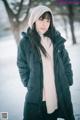 A woman standing in the snow wearing a black jacket and a white hat.