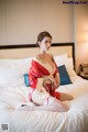 A woman in a red kimono sitting on a bed.