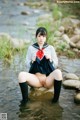 A woman in a school uniform sitting on a rock in the water.