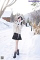 A woman in a white sweater and black skirt standing in the snow.