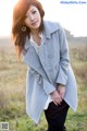 A woman in a gray coat standing in a field.