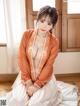 A woman in an orange kimono sitting on the floor.