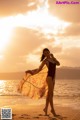 A woman in a bathing suit standing on the beach at sunset.