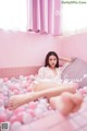 A woman laying on a bed covered in pink and white balloons.