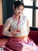 A woman in a pink and white hanbok sitting on a red couch.