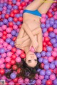 A woman in a blue bikini laying in a ball pit.