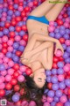 A woman in a blue bikini laying in a ball pit.