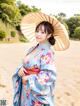 A woman in a blue kimono holding an umbrella on the beach.