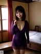 A woman in a purple dress posing in a bedroom.