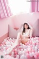 A woman in a white lingerie sitting in a pink ball pit.